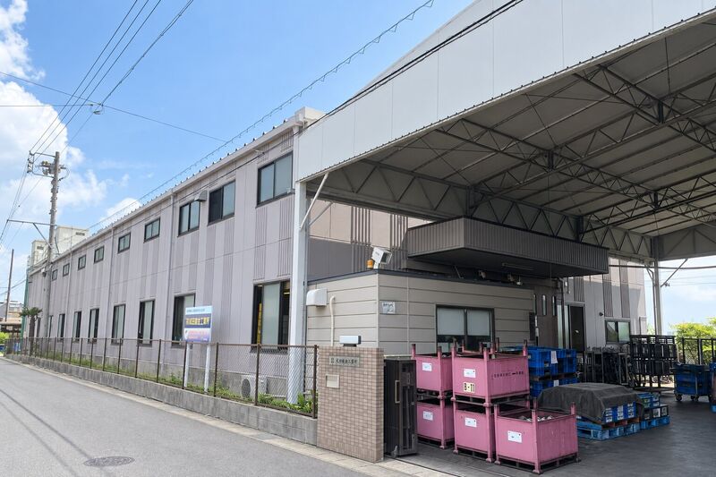道路から見た本社工場の外観。白い大屋根の荷捌き場と、2階建ての建屋